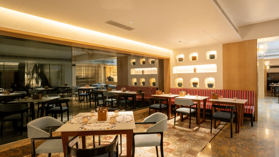 The Wild Fork at La Marvella, Bengaluru featuring dining table, chairs, and sofa. There are also flower pots  placed on the wall.