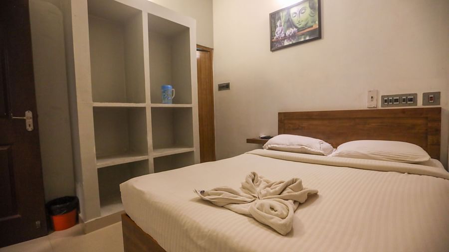 A corner view of a double bed room with plushy bed and shelves and a wall painting hanging at La  Paradise Residency  