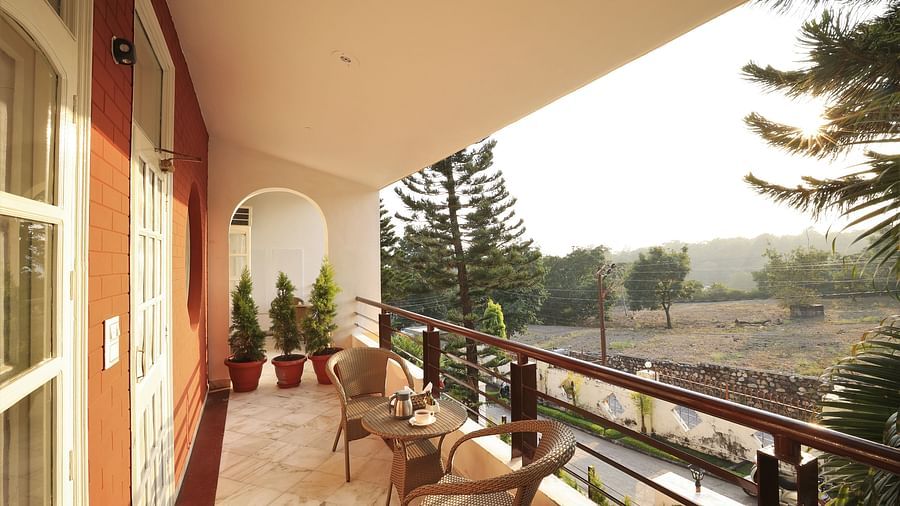 An image of a balcony where chairs are placed from where green trees and plants can be seen - Lamrin Boutique Cottages Rishikesh
