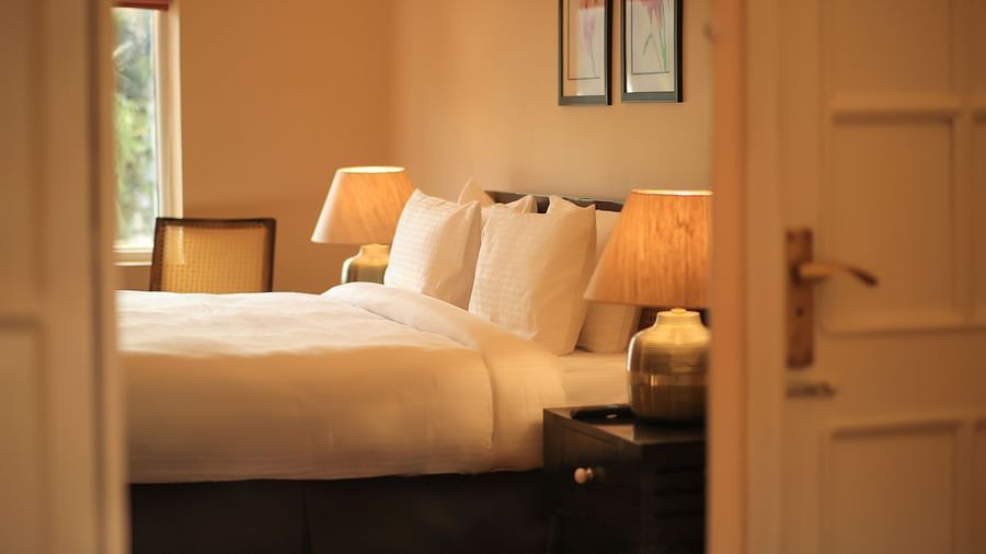A glimpse of the Super Deluxe Room 4 where a bed with pillows, an open window, and a bedside table with lamp can be seen - Lamrin Boutique Cottages Rishikesh