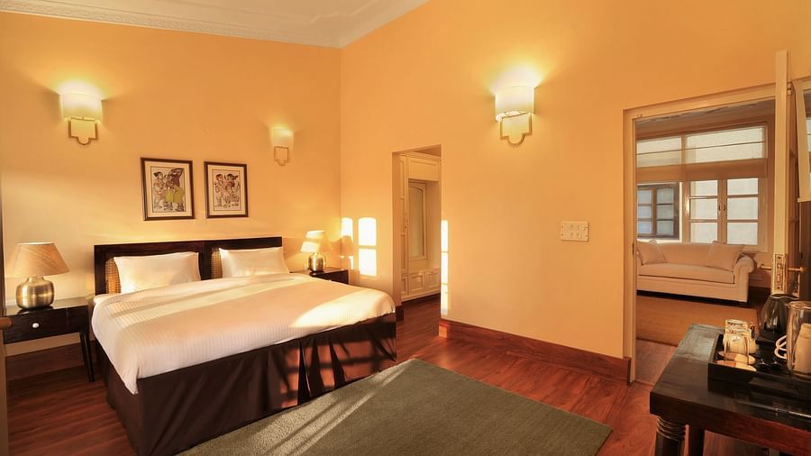 An image of a Super Deluxe room with a double size bed, bedside table with lamps on either side, and a table where antique and decorative items are placed - Lamrin Boutique Cottages Rishikesh