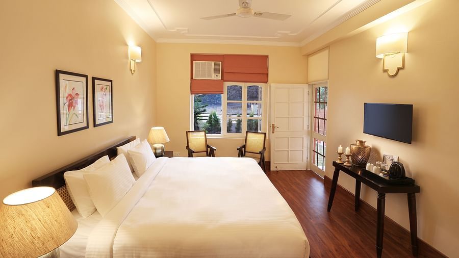 An image of a Super Deluxe Room equipped with soft bedding, modern furniture, flat TV screen, and a seating area with chairs  - Lamrin Boutique Cottages Rishikesh