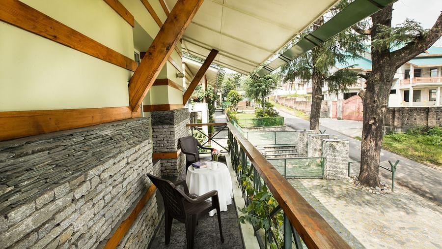 Cozy balcony setup with a small table, chairs, and a view of lush greenery and distant hills.