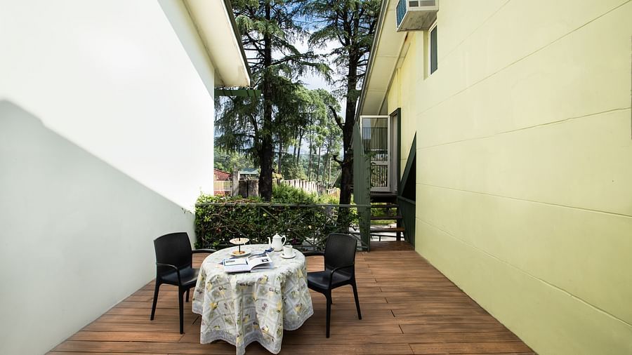 A neatly arranged balcony with a dining setup, offering a view of mountains and green lawns.