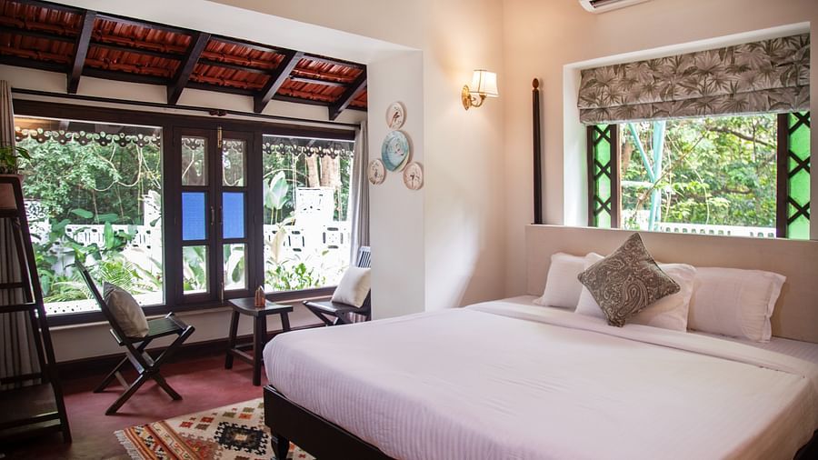 An image of a bed with big windows on the side with greenery outside at Lamrin Ucassaim Hotel, Goa