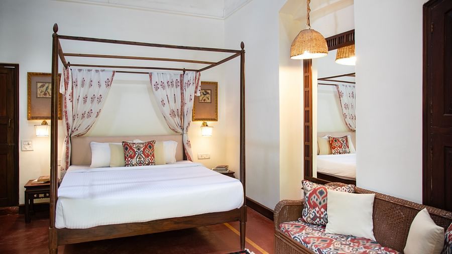 An image of a four poster bed with a sofa and bedside table on either side - Lamrin Ucassaim Hotel, Goa