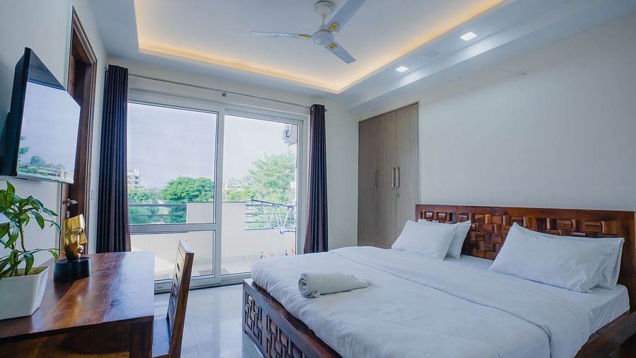 An image of a bedroom featuring a king size bed, a flat TV screen, a work desk and chair, and some flower pots - Lime Tree Hotels on Golf Course Extension Road Gurgaon