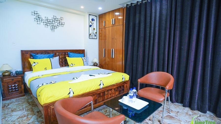 An image of a bedroom with a double size bed, a seating area with chairs and tables, a wardrobe, and a bedside table - Lime Tree Hotel Near 32nd Avenue