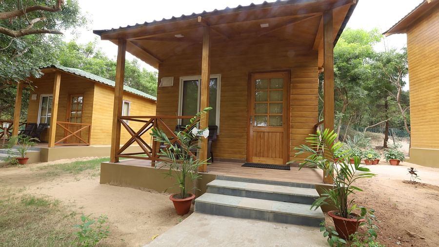 A side angle front view of wooden cabin with a charming front porch, nestled within the verdant grounds of a tranquil resort, inviting relaxation amidst nature- lotus eco beach resort konark.
