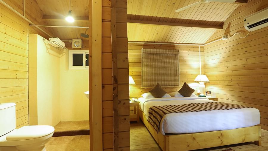  A cozy and inviting hotel room featuring wooden interiors, a plush bed, and modern amenities, with a separate seating area and an en-suite bathroom, offering comfort and style- Lotus eco beach beach resort konark.