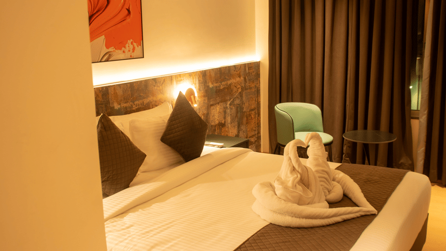 A bedroom with king size bed, bedside lamps, chair, table, wall art, and folded towel decor at Magnus Lxia Premier, Kalyani Nagar.