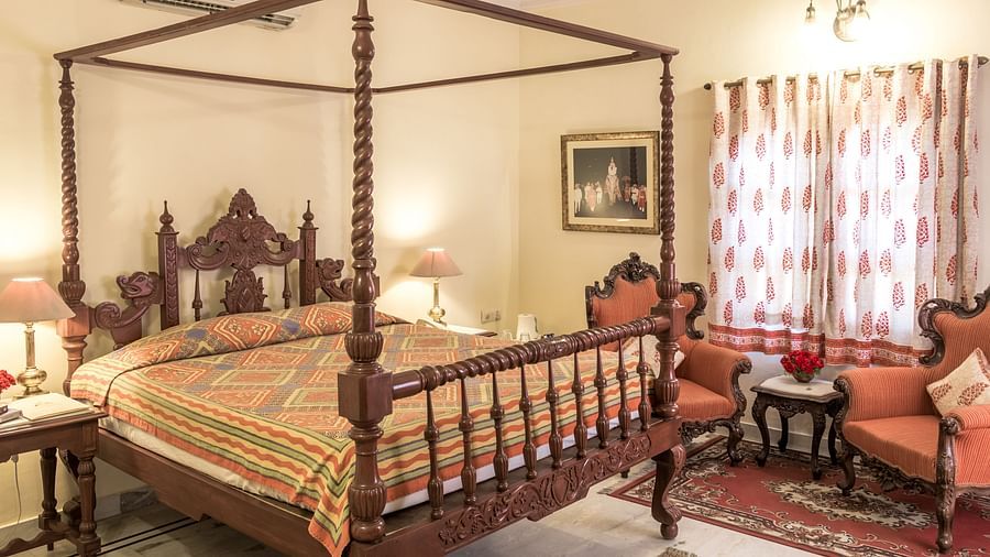 A king bed with side tables, lamps and single seater sofas next to it inside Standard rooms - Mandawa Haveli, Jaipur