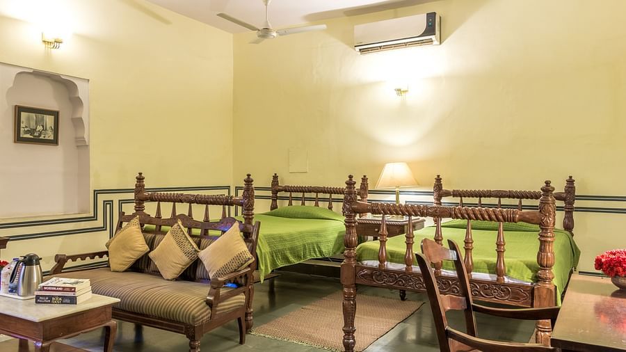 Two twin beds with a sofa and a small table in front of it inside Mandawa Haveli, Jaipur