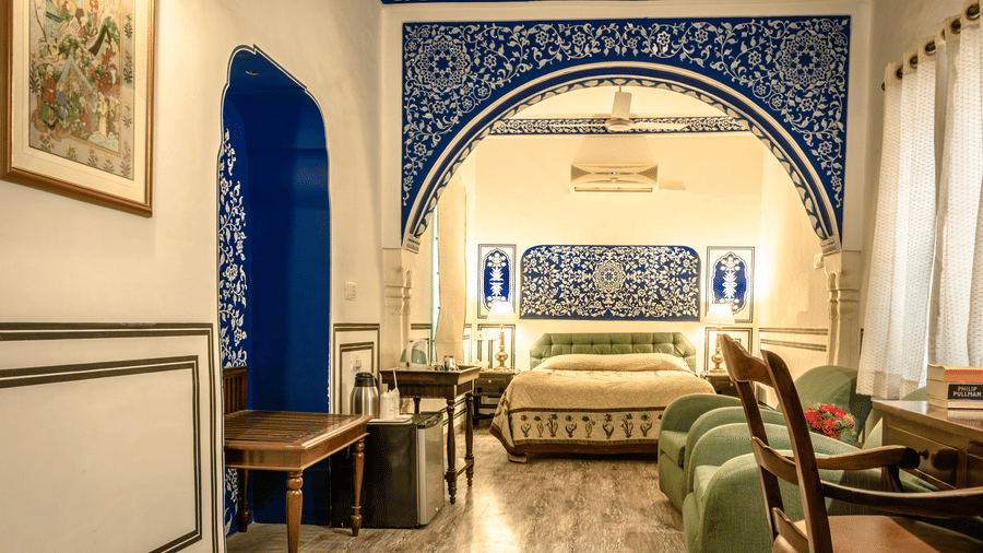 Deluxe room at Mandawa Haveli, Jaipur featuring a king size bed, a minibar, a table with tea and coffee maker, two sofa chairs, and a work desk and chair.