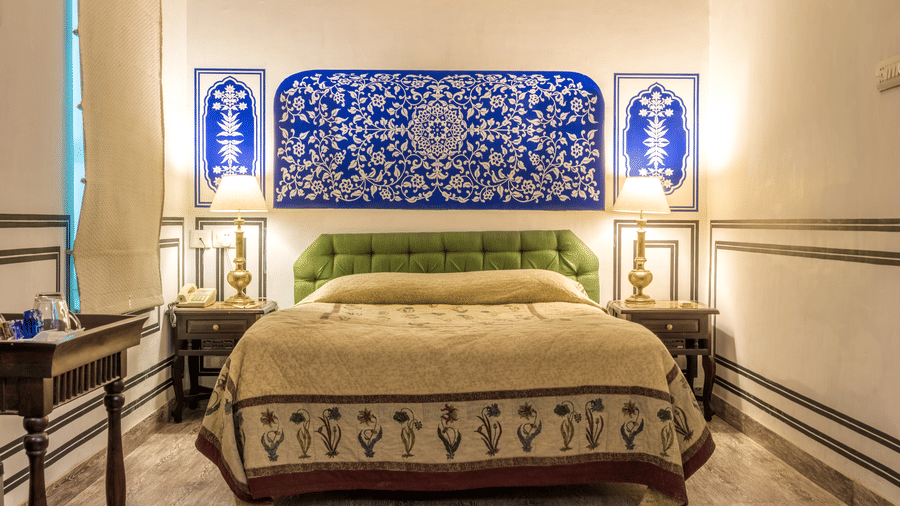 Deluxe Room at Mandawa Haveli, Jaipur featuring a king size bed, bedside table with lamps on either side, and a table with tea and coffee maker.
