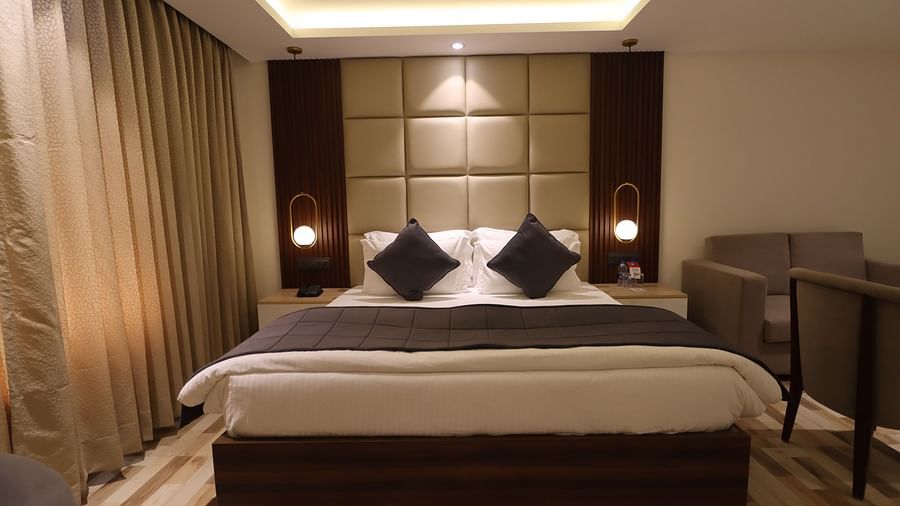 Front view of a bed with bedside tables, sofa set and partial view of the fan of studio room - Mastiff Hotel, Dhanbad 