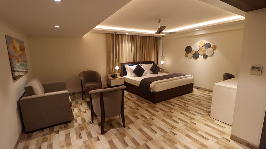 Side angle view of a Cozy bed with bed side tables, sofa set with coffee table and painting hanging over it and ceiling fan in  studio bedroom - Mastiff Hotel, Dhanbad
