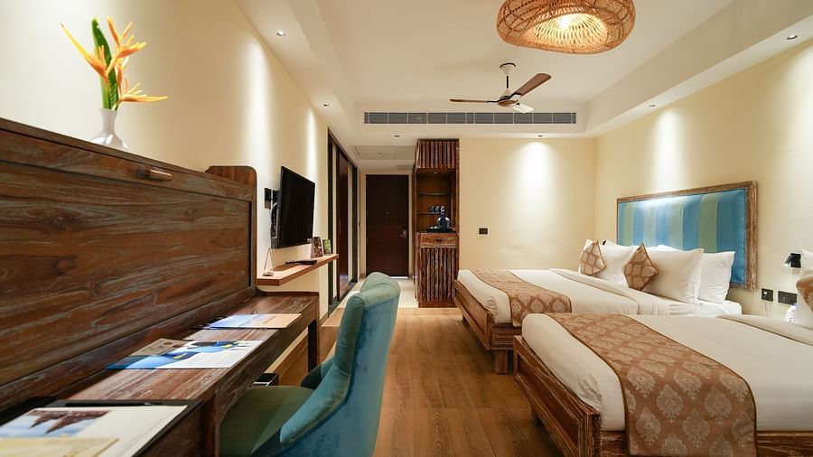 A well-lit hotel room with two twin beds, a desk, a TV, and a decorative wicker lamp - MGM Beach Resorts