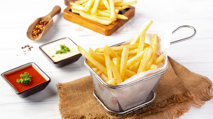 A metal basket filled with french fries is placed on a burlap mat, surrounded by small square bowls of various dipping sauces.