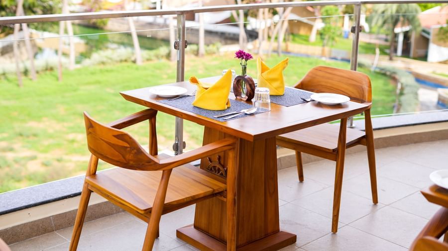 A romantic table setting for two on a balcony overlooking a lush green landscape and a pool - MGM Beach Resorts.