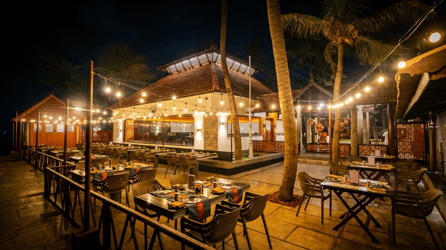 Outdoor dining area at MGM Beach Resorts restaurant illuminated with warm string lights at night, surrounded by palm trees and a tropical setting.