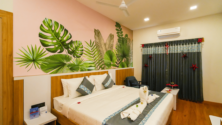 A view of the bedroom featuring a bed with a grey and white duvet, a tropical leaf mural, and a dark/red door in the background.