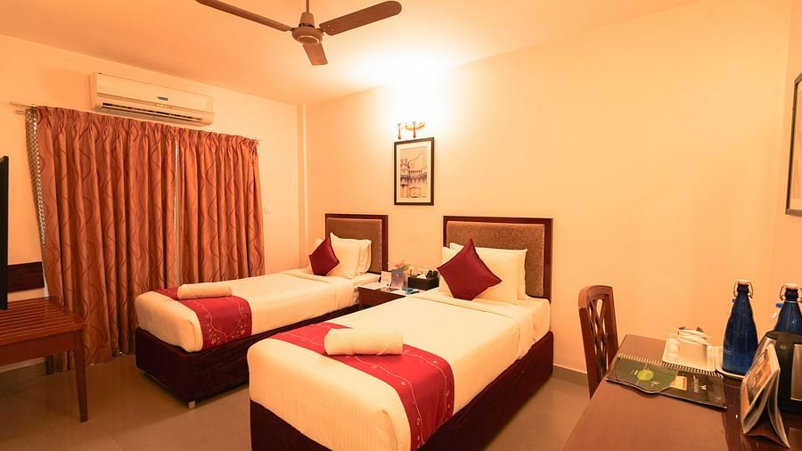 An angular shot of twin beds side by side and a table along with a chair facing the wall