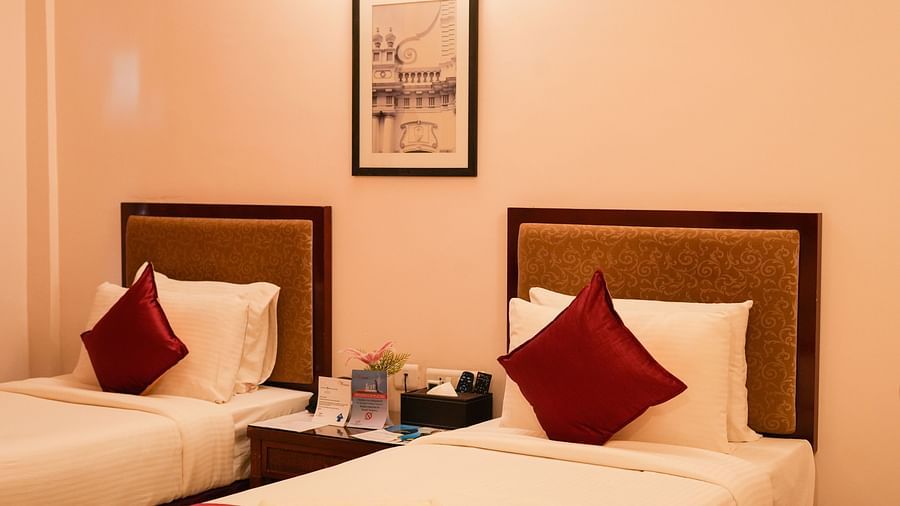 Image of twin beds with pillows and cushion with a nightstand in between and a wall hanging over it on the wall