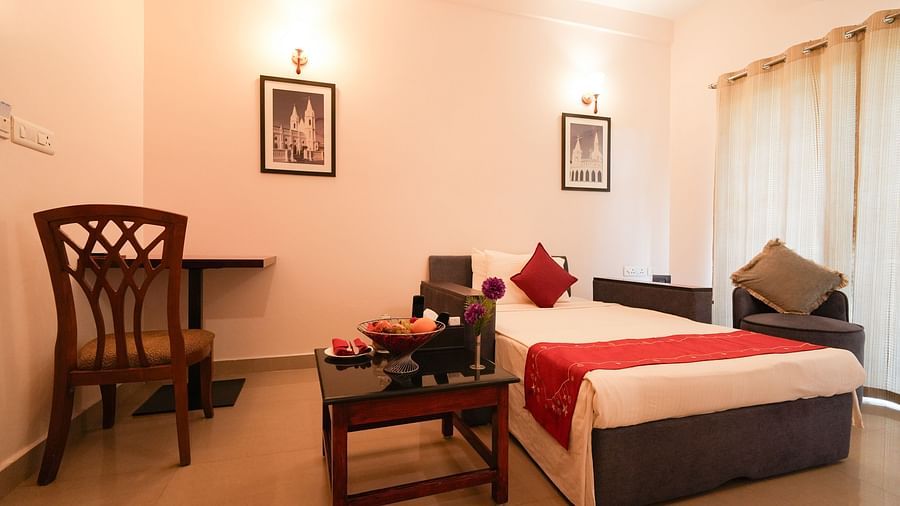 Image of Gandeur Room featuring a single bed, a coffee table and a desk with a chair next to it opposite to which is a couch