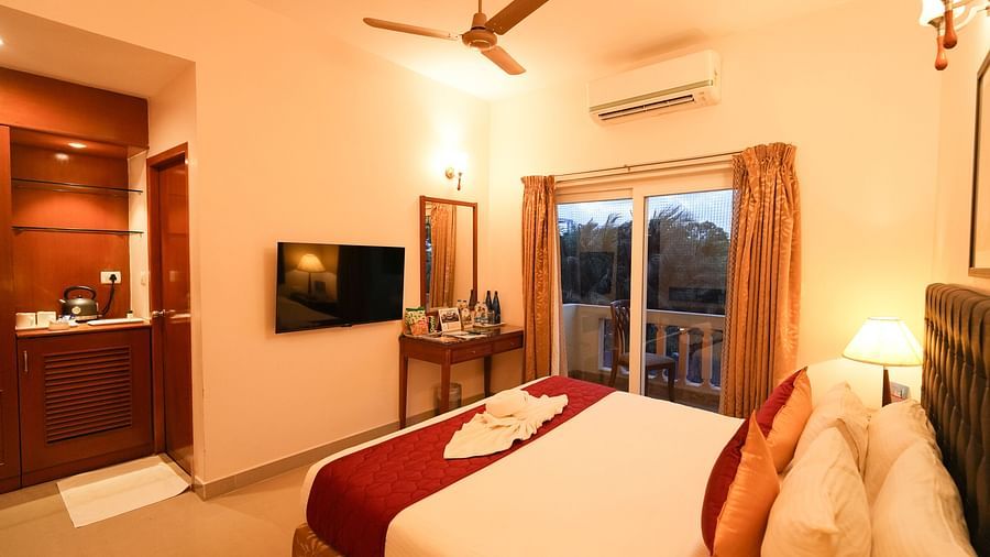 Image of Grandeur Pool View Suite featuring a plush bed facing the TV on the wall next to which is a mirror along with a dressing table beside the balcony door