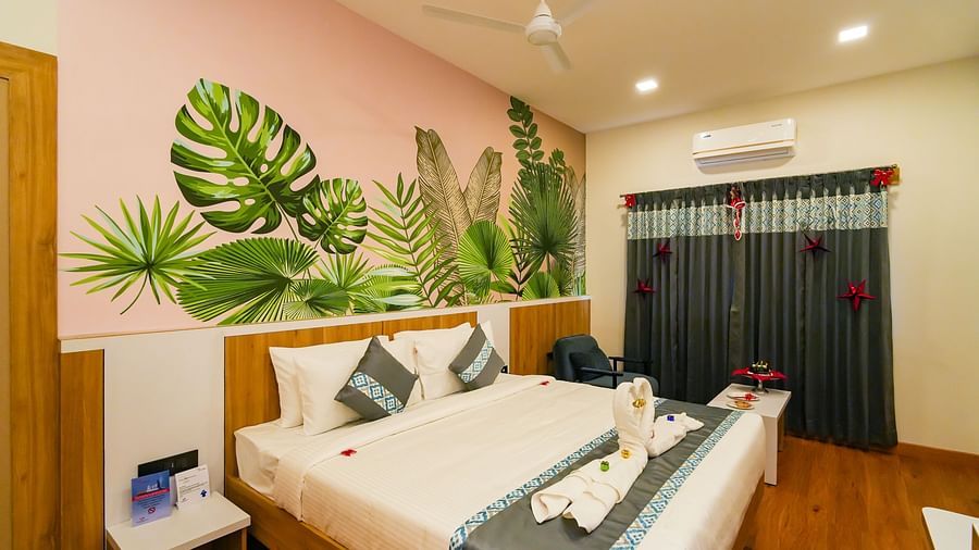 Bedroom in warm lighting featuring a plush bed with two swans made of towels on it and a nightstand next to it as well as a sitting space beside the window