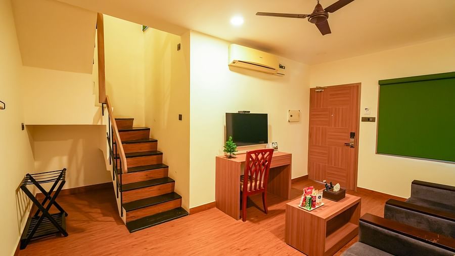 Image of a staircase leading upstairs next to which a TV and work desk along with sofa with coffee table are placed