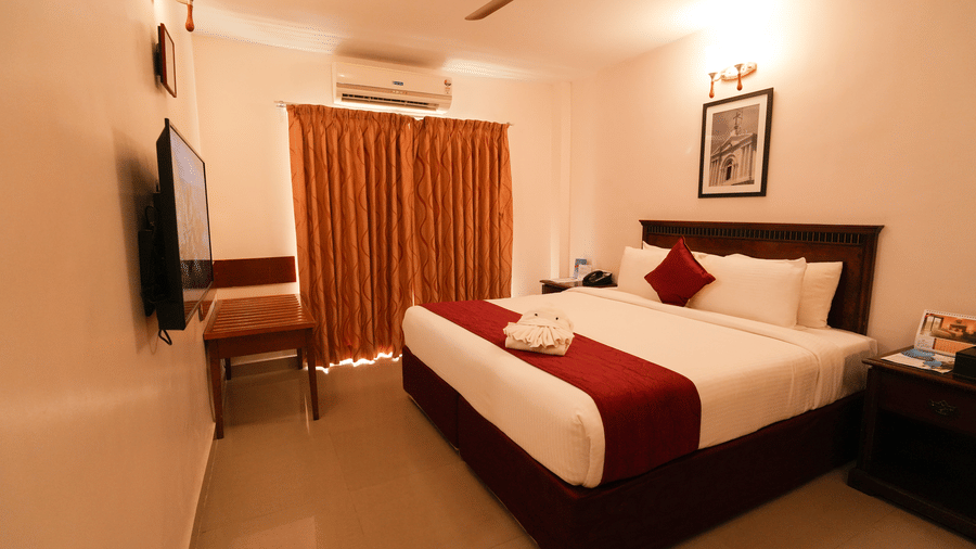 MGM Vailankanni Residency - Deluxe Room - Queen Bed. Image of the well-made bed, bedside tables, and floor-to-ceiling curtains.