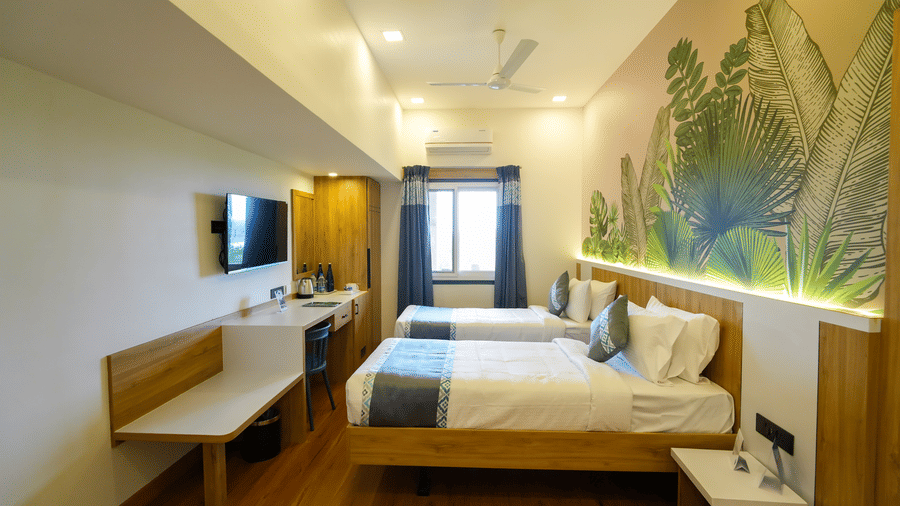 A contemporary room with two beds, light wood furniture, and a colorful mural of tropical leaves behind the beds.