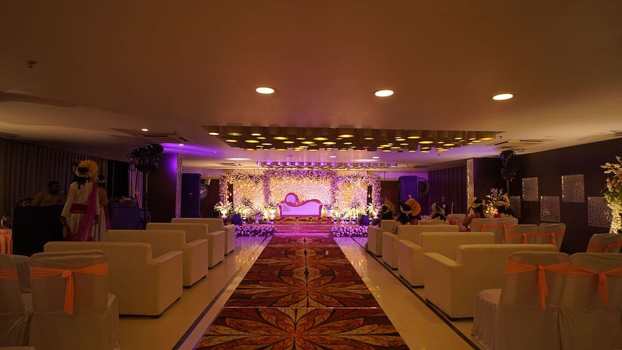 Indoor wedding venue with dramatic purple lighting and stage décor, lined with cushioned seating at Voyage Milestone Hotel and Banquet Siliguri