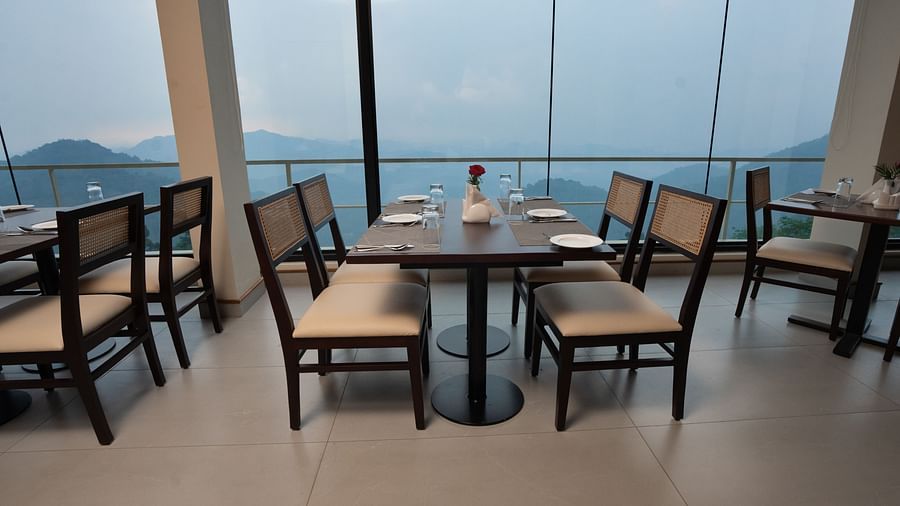Chairs and tables in a restaurant with glass windows and mountain views | Misty Queen by Dimora, Kakkadampoyil