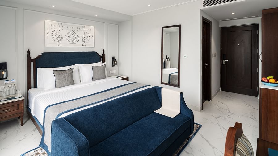 An image of a large bed with a blue bed runner, positioned in front of a work desk - MJ Sarovar Portico, Haridwar