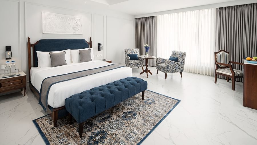 A spacious room with a large bed, carpeted floors, furniture, a work desk, and blackout curtains - MJ Sarovar Portico, Haridwar