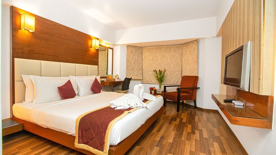 Spacious executive room with a king sized bed, wooden flooring, warm lighting, and modern amenities at Monarch Luxur Hotel, Bangalore.