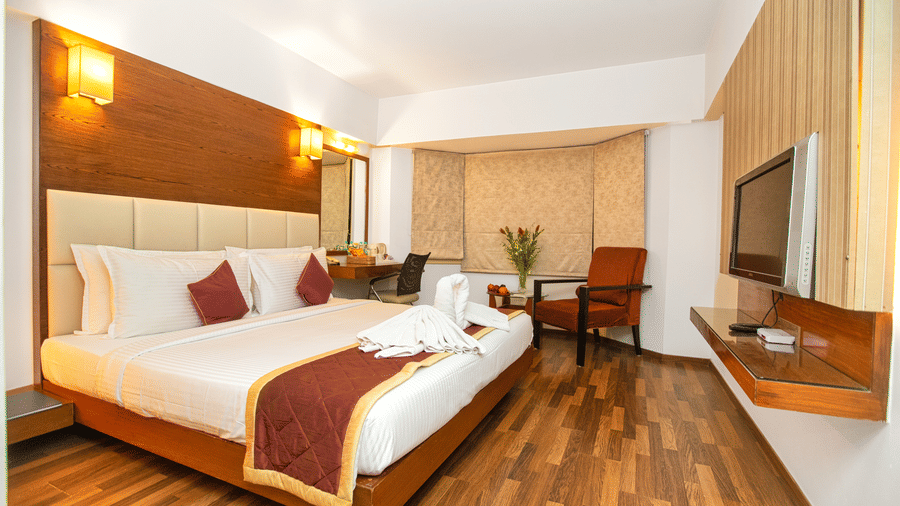 Spacious executive room with a king sized bed, wooden flooring, warm lighting, and modern amenities at Monarch Luxur Hotel, Bangalore.