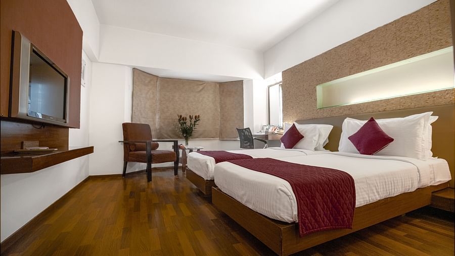 Elegant twin-bed room with contemporary decor, wooden flooring, and a cosy seating area at Monarch Luxur Hotel, Bangalore.
