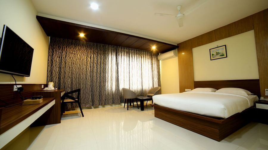 A room with neat bed sofa chairs and study desk and a TV - Mysore Gate Hotel Bangalore