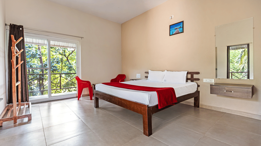Side view of a clean, minimalist hotel room with tiled floors, a double bed, and natural light from large windows - Nature Trails Ashoka Resort Hampi