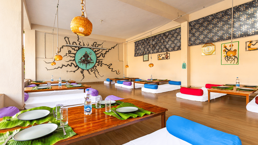 Low-angle view of a restaurant table set with banana leaves and steel plates, featuring colorful bolster cushions - Nature Trails Ashoka Resort Hampi