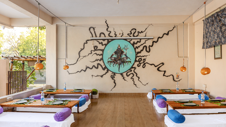 Wide shot of a dining hall with symmetrical floor seating and a prominent black-and-teal wall mural - Nature Trails Ashoka Resort Hampi