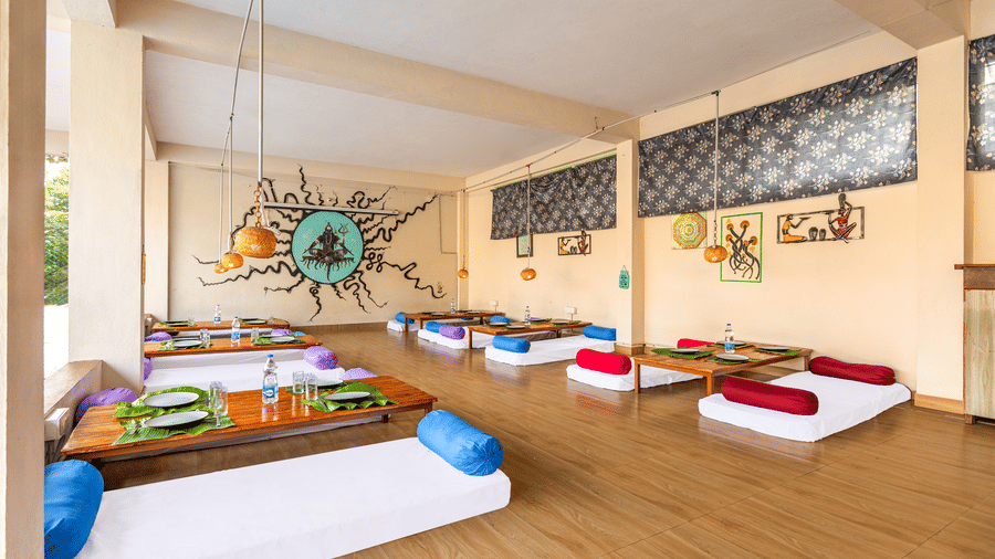 Indoor dining area featuring traditional floor seating, wooden tables, and a large sun-themed mural on the wall - Nature Trails Ashoka Resort Hampi