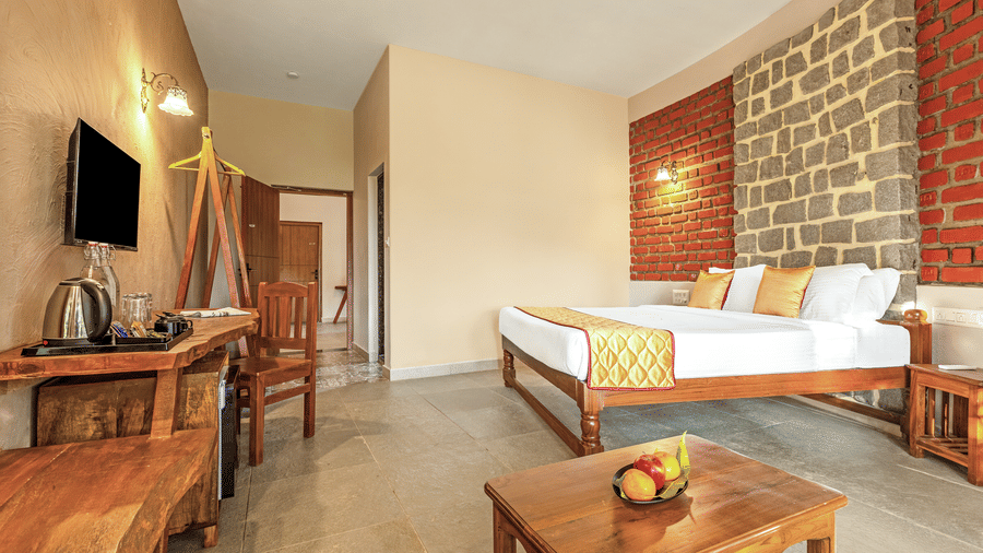 Premium bedroom featuring an exposed brick accent wall, wooden desk, and warm lighting - Nature Trails Ashoka Resort Hampi