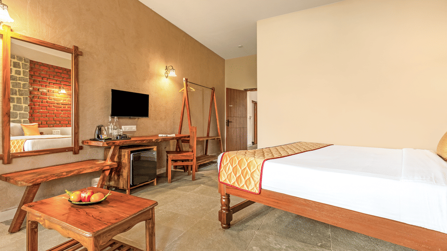 View of the room's workspace including a wooden desk, mini-fridge, and large vanity mirror - Nature Trails Ashoka Resort Hampi