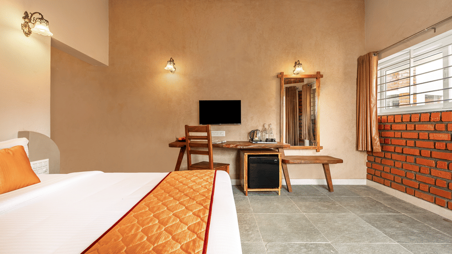 Well-lit premium room with an orange-themed bed runner and views of the red-brick exterior - Nature Trails Ashoka Resort Hampi