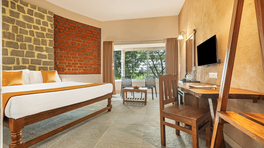 Spacious cottage interior with a stone-cladded wall and large windows - Nature Trails Ashoka Resort Hampi